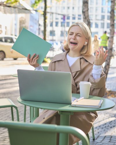 Portrait of upset, crying young woman, sitting with laptop, sobbing from failure and disappointment, failing something, having mental breakdown on street. Lifestyle and emotions concept